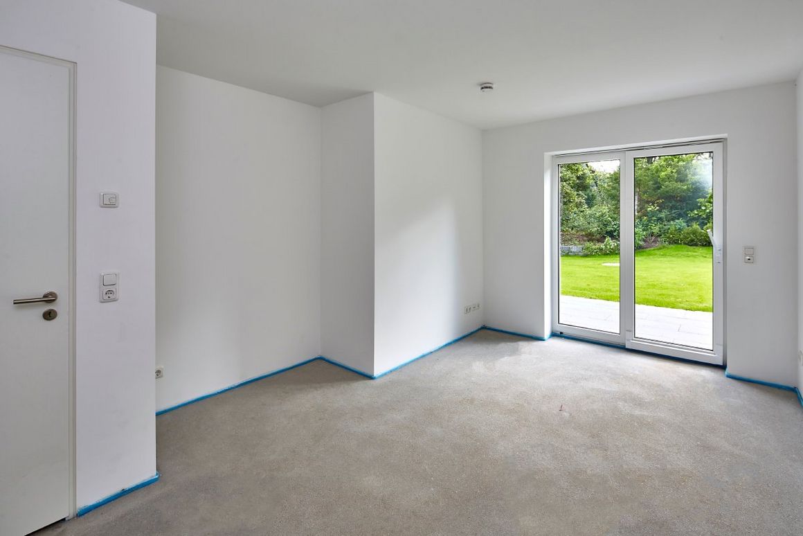 Leerer Raum mit Estrich und Blick in den Garten.